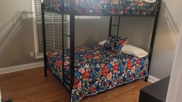 A bunk bed with floral bedding, a window with blinds, and a wooden floor.