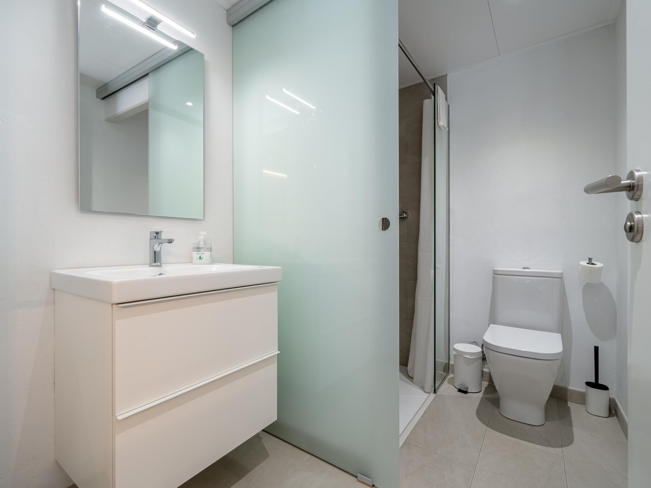 A modern bathroom with a white vanity, a mirror, a toilet, and a shower area.