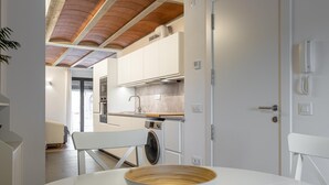 A modern kitchen with white cabinets, a wooden ceiling, and a white dining table with a bowl.