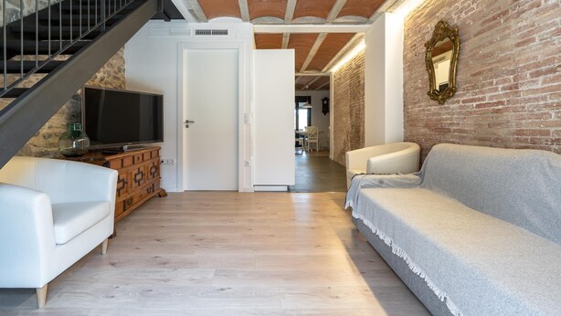 A modern living room with a staircase, a television, and a brick wall.