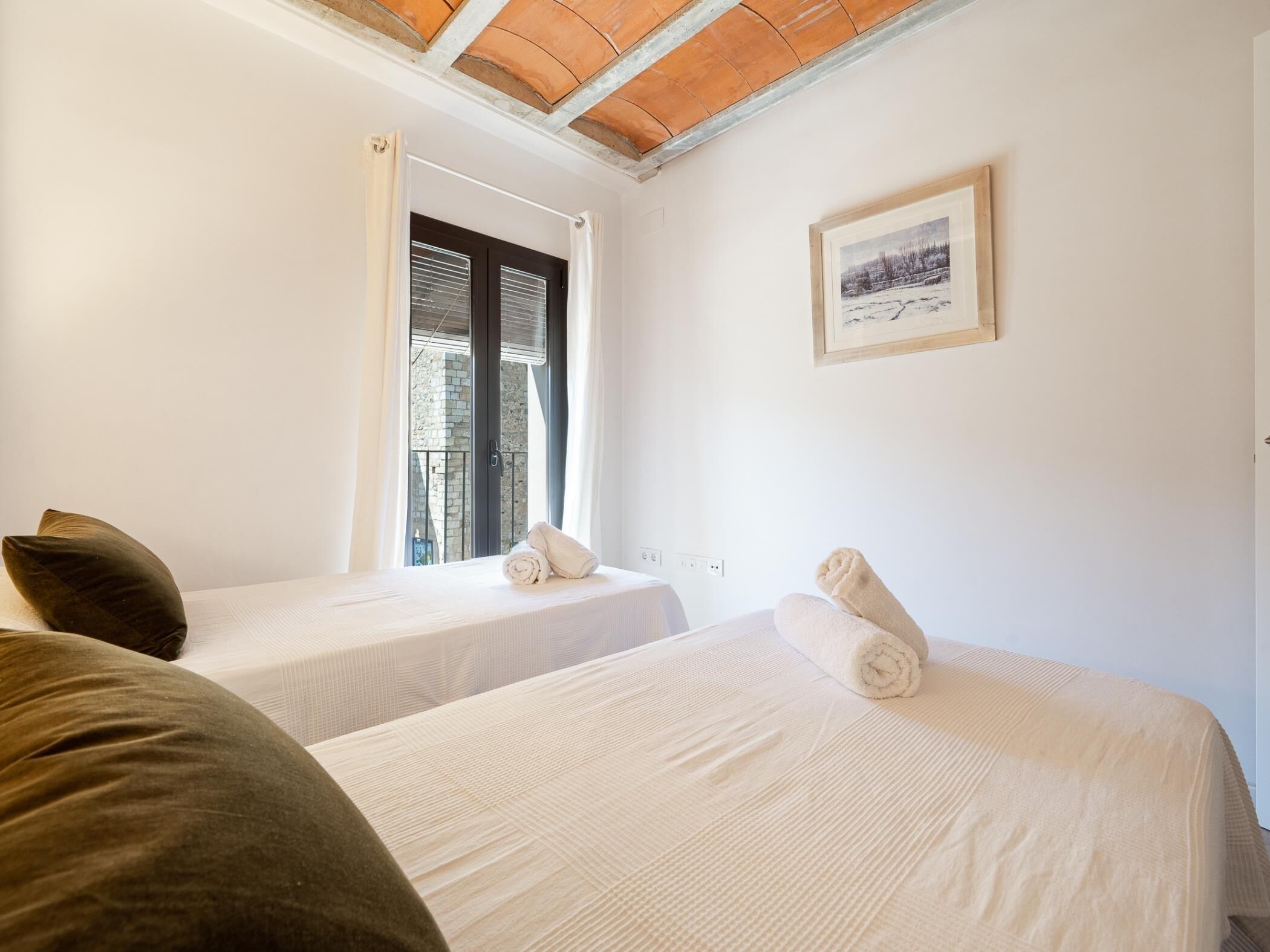 Habitación de hotel con dos camas, una ventana con cortinas, un cuadro enmarcado en la pared y techo de madera.