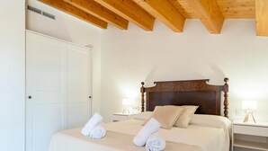 Une chambre avec un plafond en bois, un grand lit avec une tête de lit, deux tables de chevet avec des lampes et une armoire blanche.