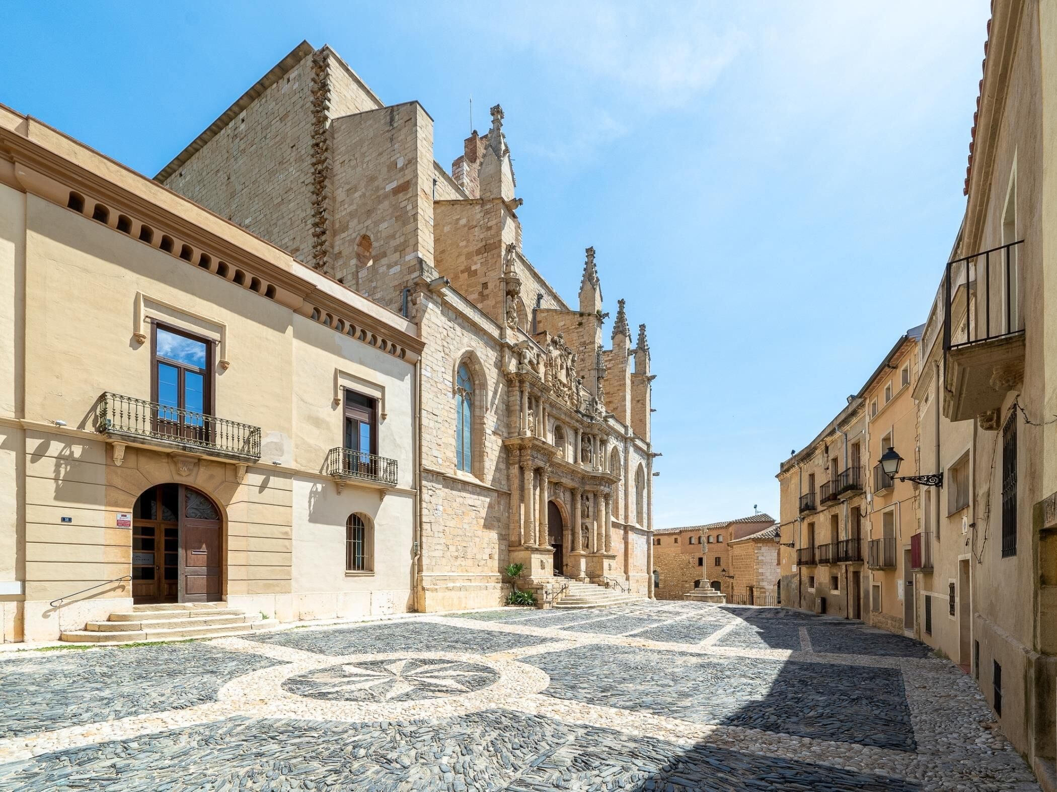 Une rue pavée bordée de bâtiments historiques, dont une église remarquable à l’architecture riche et élaborée.