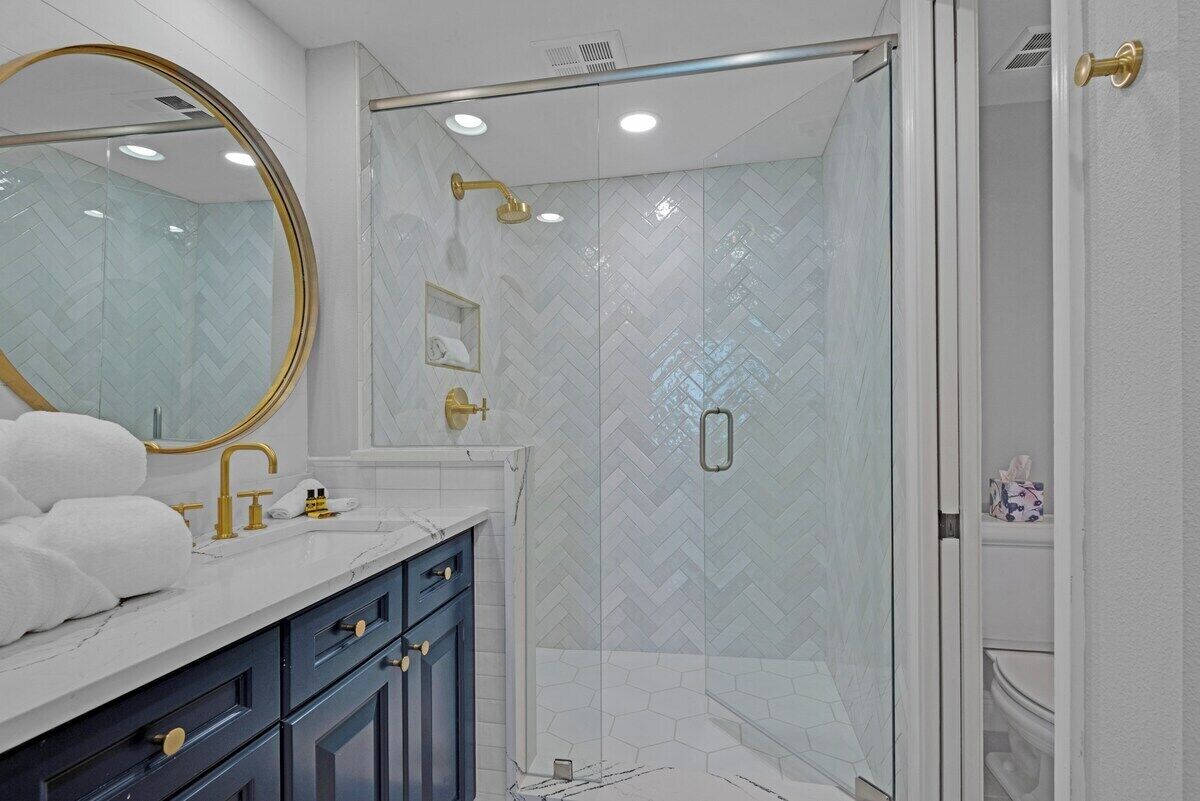 A modern bathroom with a glass-enclosed shower, a large mirror, and a marble countertop.