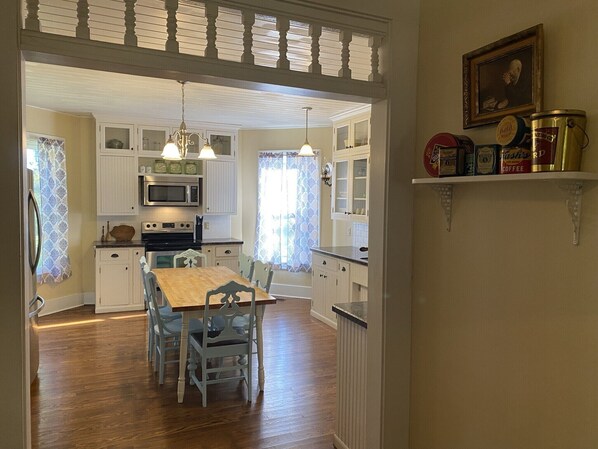 Une cuisine avec des meubles de rangement en bois, une table à manger et des chaises. On y trouve un four à micro-ondes, une cuisinière et un luminaire suspendu.