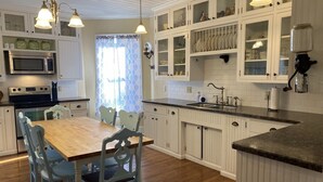 A kitchen with white cabinets, a wooden dining table, and chairs. There is a microwave, a sink, and a stove.