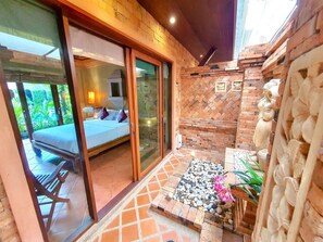 Quarto com cama, banheiro com chuveiro e pequena área externa com mesa e cadeiras.