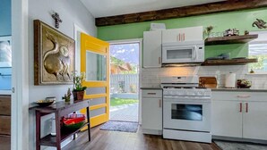 Een keuken met witte kasten, een magnetron, een oven en een houten tafel met een kom en een bloempot.