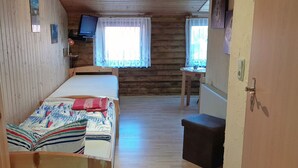 Ein Zimmer in einer Holzhütte mit einem Bett, einem kleinen Tisch, einem Fernseher und einem Fenster mit Vorhängen.