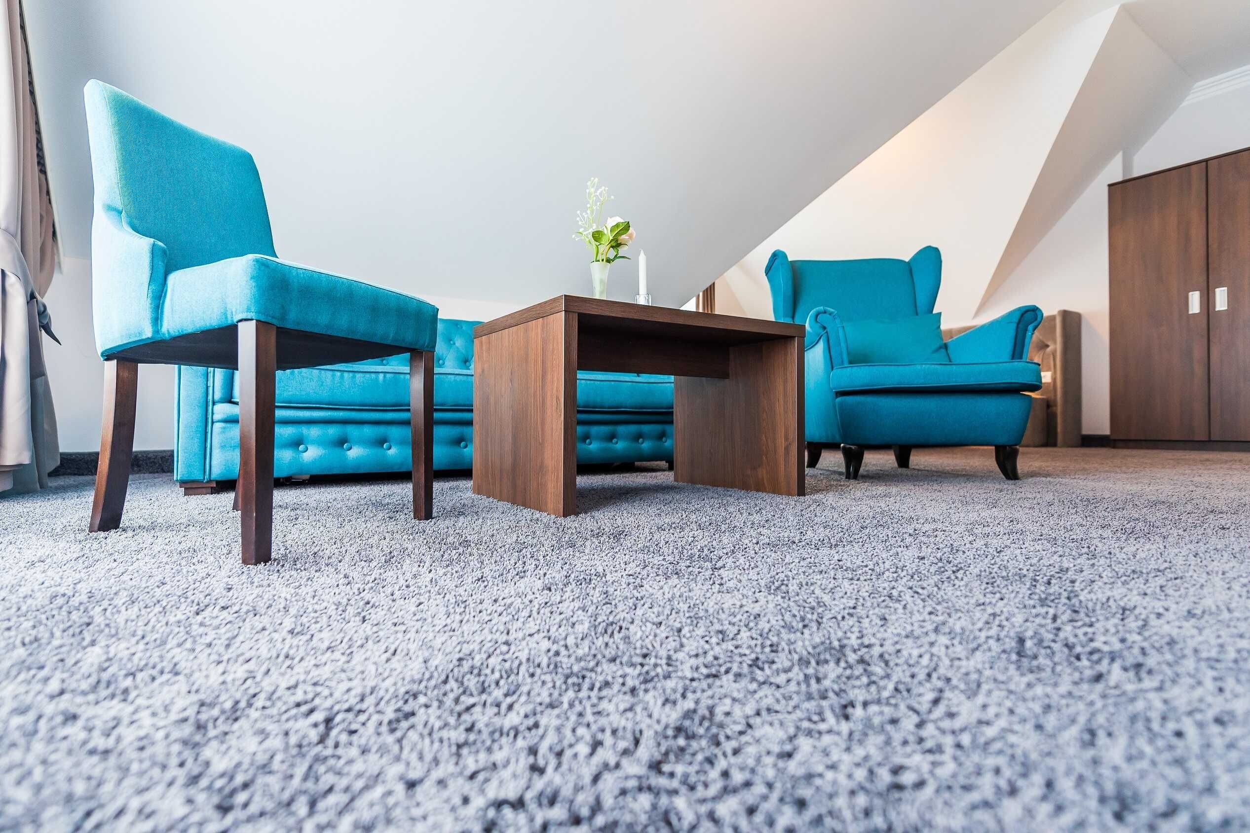 Ein Zimmer mit einem blauen Sofa, zwei gleichgestimmten Sesseln, einem Holztisch und einer Blumenvase.
