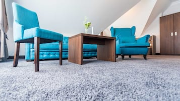 Ein Zimmer mit einem blauen Sofa, zwei gleichgestimmten Sesseln, einem Holztisch und einer Blumenvase.