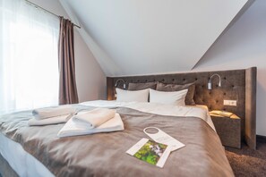 A neatly made bed with pillows and a folded towel, a bedside table with a lamp, and a window with curtains.