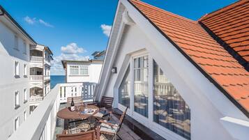 Un balcon avec une table et des chaises, une vue sur la mer et un bâtiment avec un toit rouge.