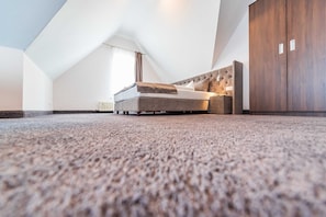 A modern loft bedroom with a high ceiling, a large bed, a wardrobe, and a radiator. - Junior Suite with Balcony - Hotel Villa Belvedere (Binz)