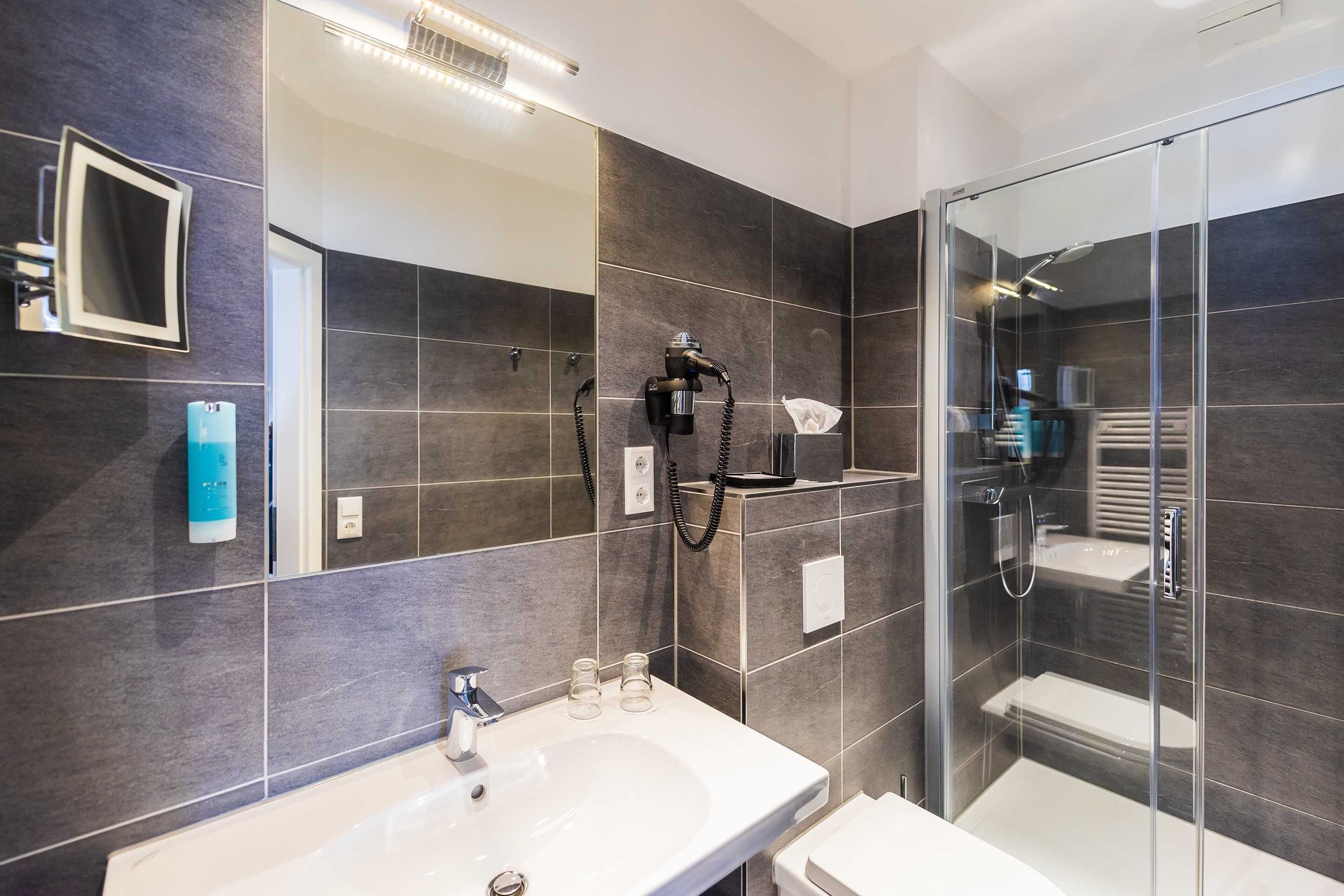 Une salle de bain moderne avec une douche à parois de verre, un grand miroir et un lavabo blanc.