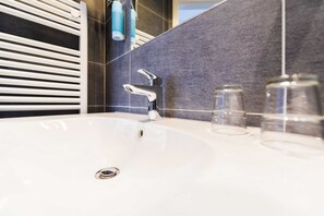 Un baño moderno con lavamanos blanco, grifo cromado y paredes de azulejos oscuros.