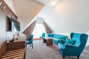 A modern room with a TV, sofa, chairs, and a small table. - Junior Suite with Balcony - Hotel Villa Belvedere (Binz)