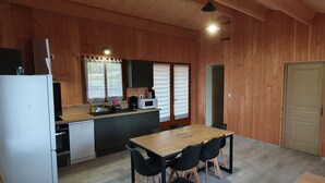 Une cuisine compacte équipée d’un réfrigérateur, d’un four à micro-ondes et d’un évier. On y trouve une table à manger avec des chaises et un banc.