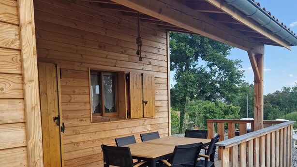 Une terrasse en bois avec une table et des chaises, une porte en bois et une fenêtre.