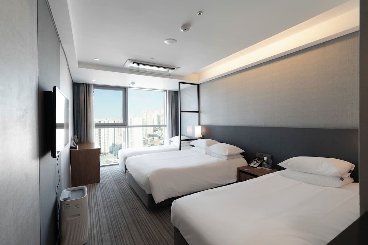 A hotel room with two beds, a desk, a chair, a TV, and a view of the city.