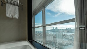 Un baño moderno con una bañera grande, una ventana con vista a la ciudad y un perchero con dos toallas.