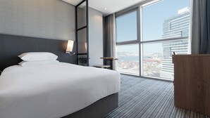 A modern hotel room with a large bed, a desk, and a view of a cityscape through a large window. - North Harbor Hotel Busan (Busan)