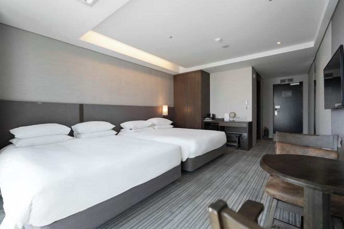 A modern hotel room with two beds, a desk, and a dining table.