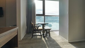 Una habitación de hotel con un ventanal grande, un escritorio de madera, una silla y una mesita redonda.