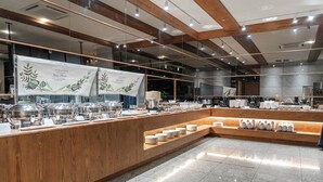 Una mesa de desayuno buffet moderna con una barra de madera, distintos recipientes de comida y un suelo de baldosas.