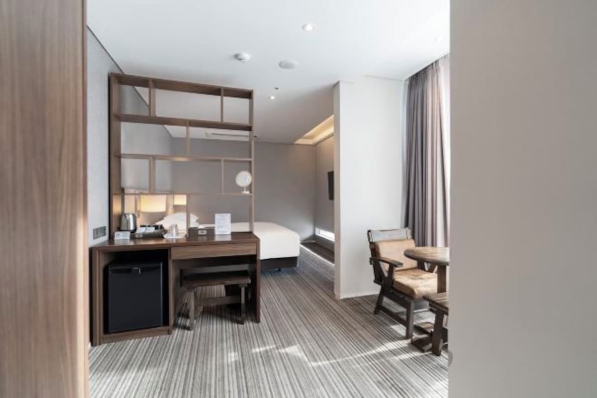 A modern hotel room with a bed, a desk, a chair, and a small table.