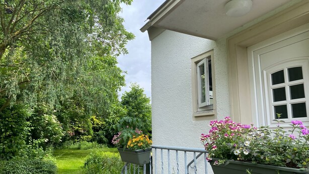 A house with a white exterior, a small window, and a door. There are two flower planters on the porch with various flowers. - Vacation apartment Heimsoth Kappeln OG - Holiday apartments Heimsoth in Kappeln (Kappeln)