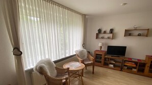 A living room with two wicker chairs, a small round table, a TV on a wooden stand, and shelves with decorative items. - Vacation apartment Heimsoth Kappeln OG - Holiday apartments Heimsoth in Kappeln (Kappeln)