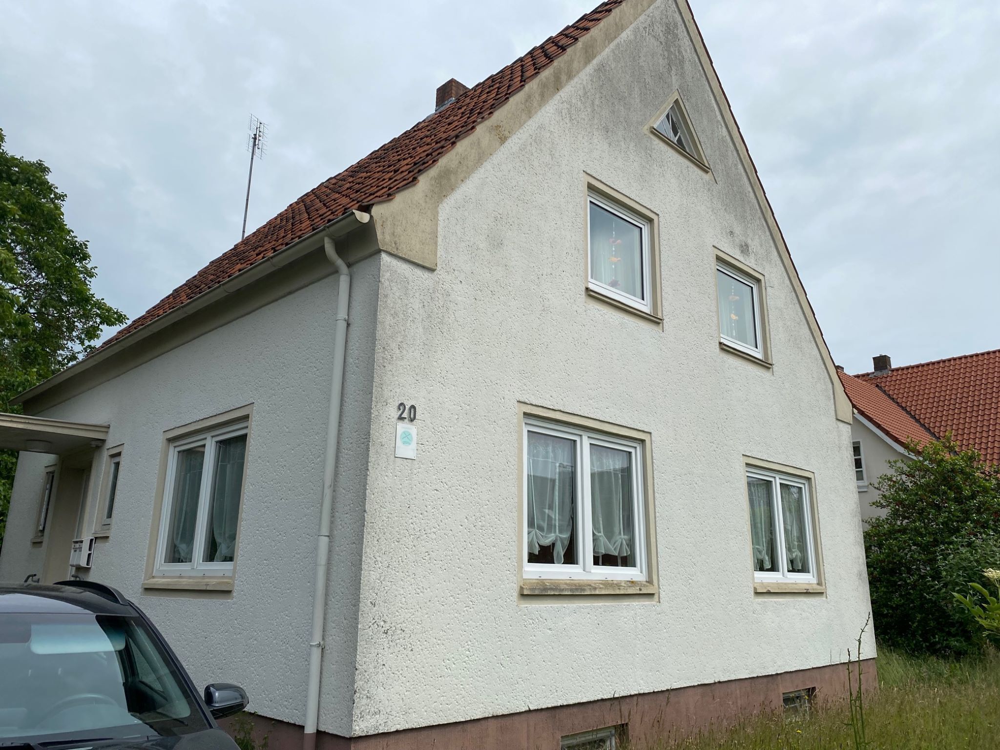 Een twee verdiepingen tellend huis met het nummer '20' aan de zijkant, een pannendak en meerdere ramen.