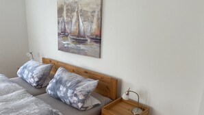 A bedroom with a wooden bed, grey floral bedding, a nightstand with a lamp, and a painting of sailboats on the wall. - Apartment Heimsoth Kappeln EG - Apartments Heimsoth in Kappeln (Kappeln)