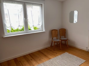 Ein Zimmer mit Holzboden, einem weißen Teppich, zwei Holzstühlen und einem Fenster mit Vorhängen.