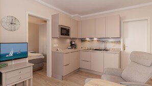 A compact kitchenette with a microwave, coffee maker, and sink. There is a television on a stand, a chair, and a small table. - FW 39, apartments on the beach - max. 3 persons - FeWo Am Strand / (Kühlungsborn)