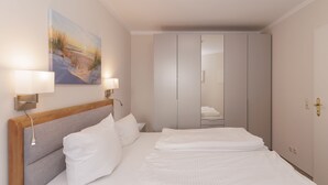 A hotel room with a large bed, bedside lamps, a painting on the wall, and a wardrobe with a mirror. - FW 39, apartments on the beach - max. 3 persons - FeWo Am Strand / (Kühlungsborn)