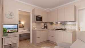 A compact kitchenette with a microwave, a sink, and a small countertop. There is a television mounted on the wall, and a bed with a view of the beach is visible through an open door. - FW 39, apartments on the beach - max. 3 persons - FeWo Am Strand / (Kühlungsborn)