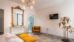 A hotel room with a bed, a large mirror, a television, a plant, and a chair. - Alma Suite - Two Bedroom Apartment, Sleeps 6 (Noto)