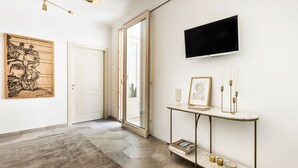 A modern interior with a large wooden artwork, a television mounted on the wall, a marble console table, and a patterned rug. - Alma Suite - Two Bedroom Apartment, Sleeps 6 (Noto)