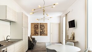 A modern kitchen with a built-in stove, a dining area with a round table and chairs, and artwork on the walls. - Alma Suite - Two Bedroom Apartment, Sleeps 6 (Noto)