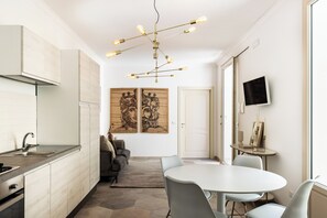 Eine moderne Küche mit Einbauherd, ein Essbereich mit rundem Tisch und Stühlen sowie Kunstwerken an den Wänden.