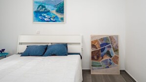 Makuuhuone, jossa on sänky, kaksi tyynyä, maalattu merimaisema ja mosaiikkitaideteos.