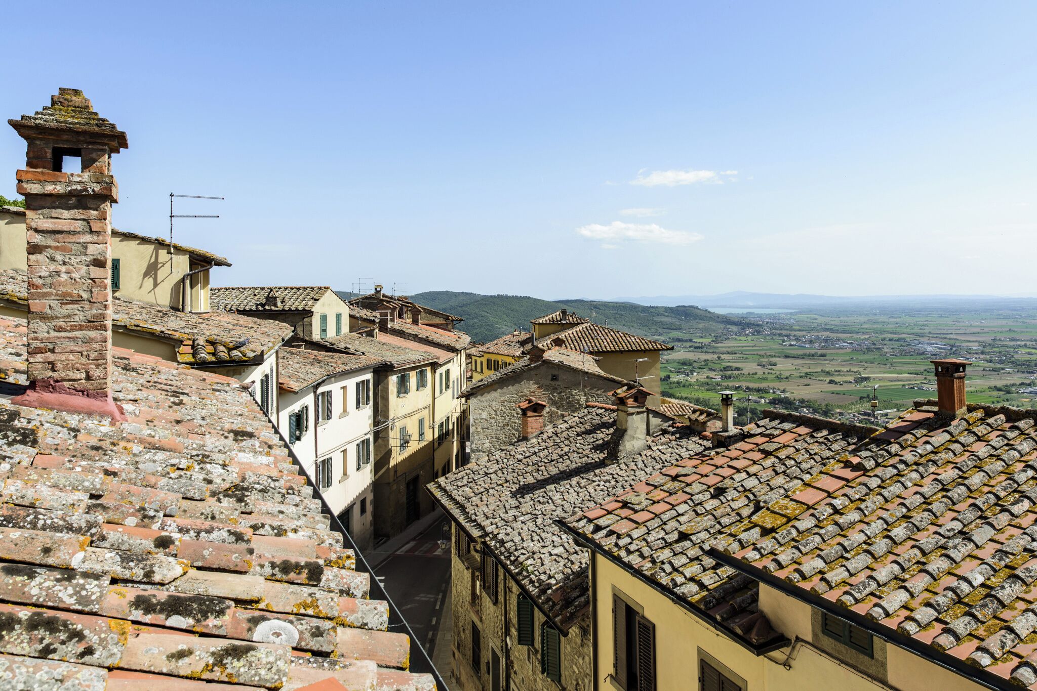 Una calle estrecha con edificios tradicionales, techos de piedra y una vista despejada del campo.