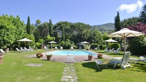 A pool area with lounge chairs and umbrellas, surrounded by greenery and hills. - Holiday apartment with outdoor pool and WiFi (Cortona)