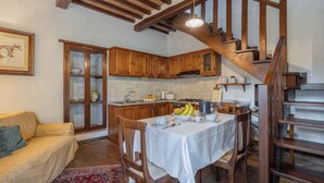 A cozy kitchen with wooden cabinets, a dining table set for two, and a staircase leading to an upper level. - Holiday apartment with outdoor pool and WiFi (Cortona)
