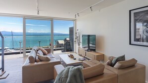 A modern living room with a large window overlooking a coastal view, a flat-screen TV, and a minimalist design.