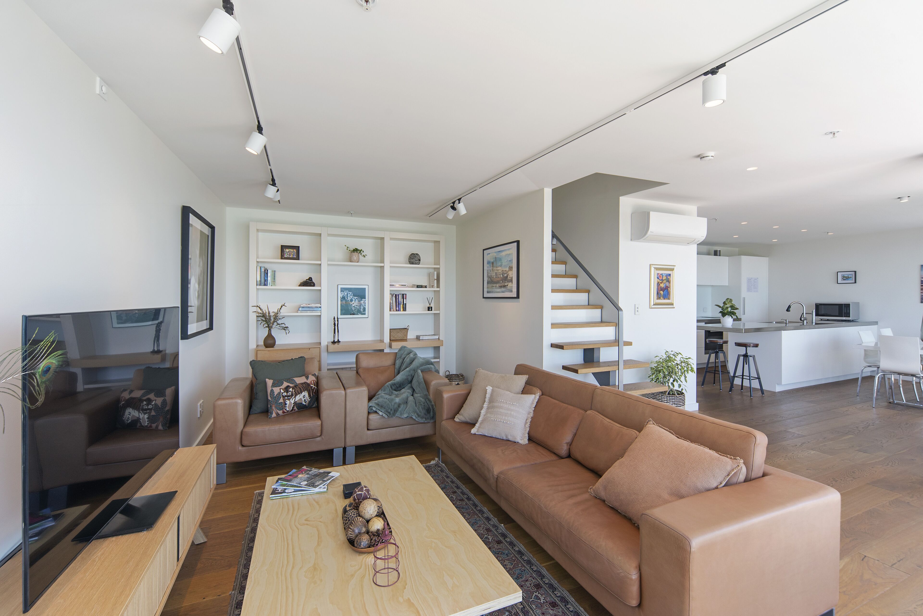 Ein modernes Wohnzimmer mit einer braunen Ledersofa, einem Holztisch und einem Bücherregal.