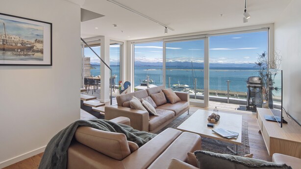 A modern living room with a large window overlooking a marina and the sea.