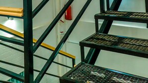 A multi-level metal staircase with wooden handrails, surrounded by white walls and a green curtain. - Nomad - Hostel (Bishkek)